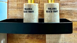 Twee Volamia Beach Front flessen op een zwart schap voor een houten muur.