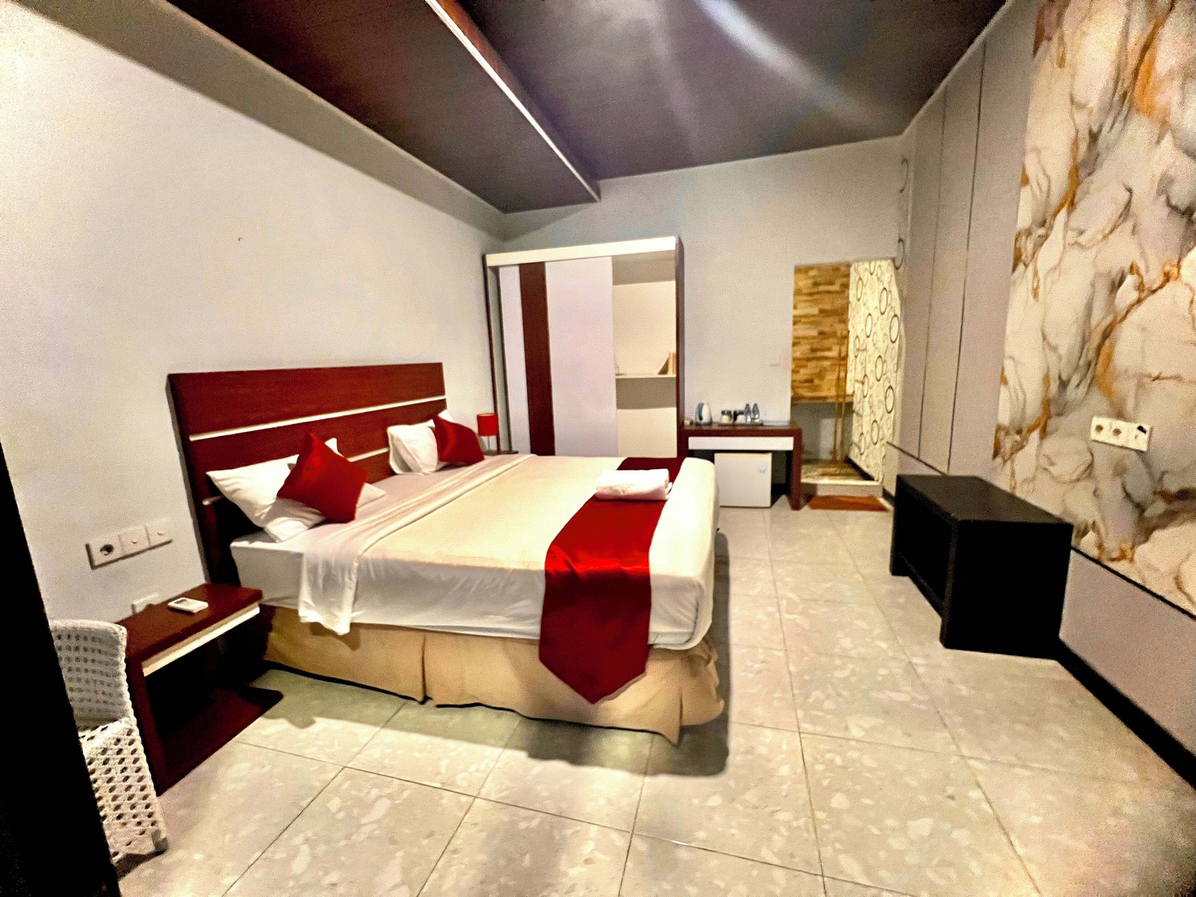 Een moderne hotelkamer met een groot bed, een nachtkastje, een spiegel, een klein bureau en een wand met een marmerachtig patroon.