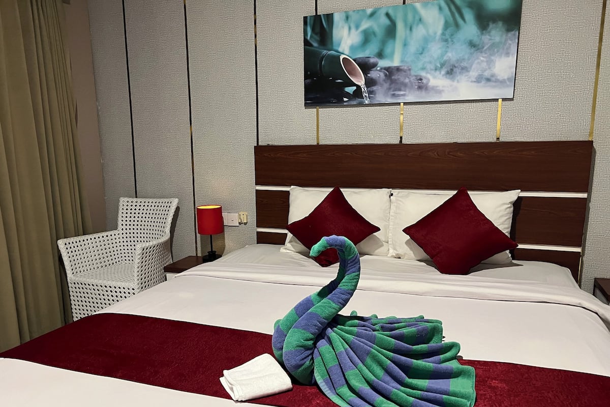 A neatly made bed with a decorative swan towel, a red throw blanket, and two red pillows.