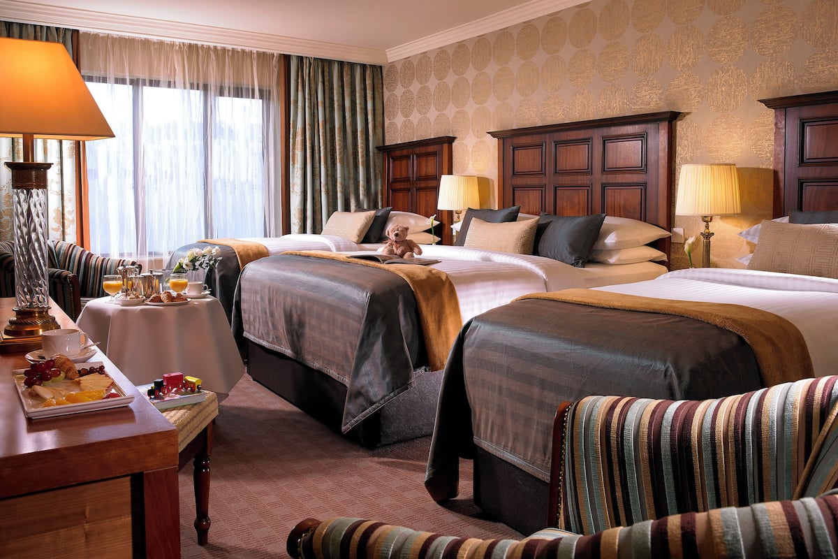Ein Hotelzimmer mit drei Betten, einem Esstisch mit Frühstück und Blick auf die Stadt.