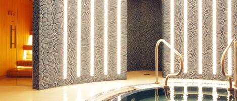 A modern indoor pool area with a mosaic wall and a glass-enclosed section.