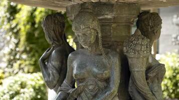 Eine Steinskulptur einer Frau, die ein Kind trägt, mit einer Säule und einer weiteren Figur im Hintergrund.