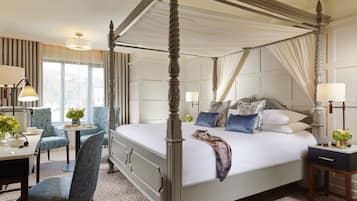 A four-poster bed with a canopy, a desk with a chair, and a small table with a vase of flowers.