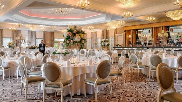 Une salle de banquet avec des tables rondes, des nappes blanches et des chaises dorées.