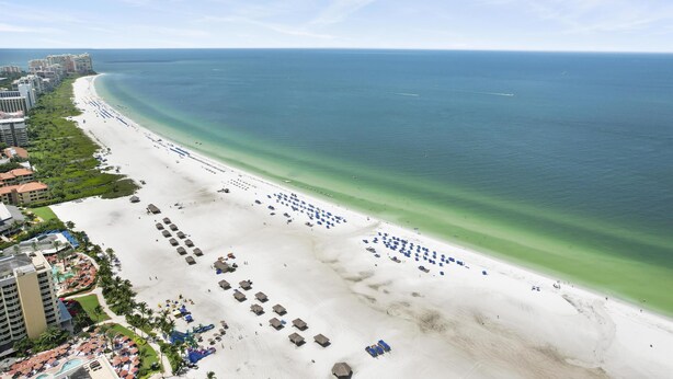 A beach resort with a long sandy beach, numerous umbrellas, and a clear view of the ocean. - Top-Rated Marco Beach House, Heated Pool, Bikes, Walk to Beach & JW Marriott (Marco Island)