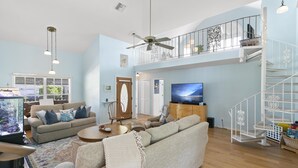 A spacious living room with a high ceiling, a large flat-screen TV, a cozy sofa set, a wooden coffee table, and a decorative fish tank. - Top-Rated Marco Beach House, Heated Pool, Bikes, Walk to Beach & JW Marriott (Marco Island)