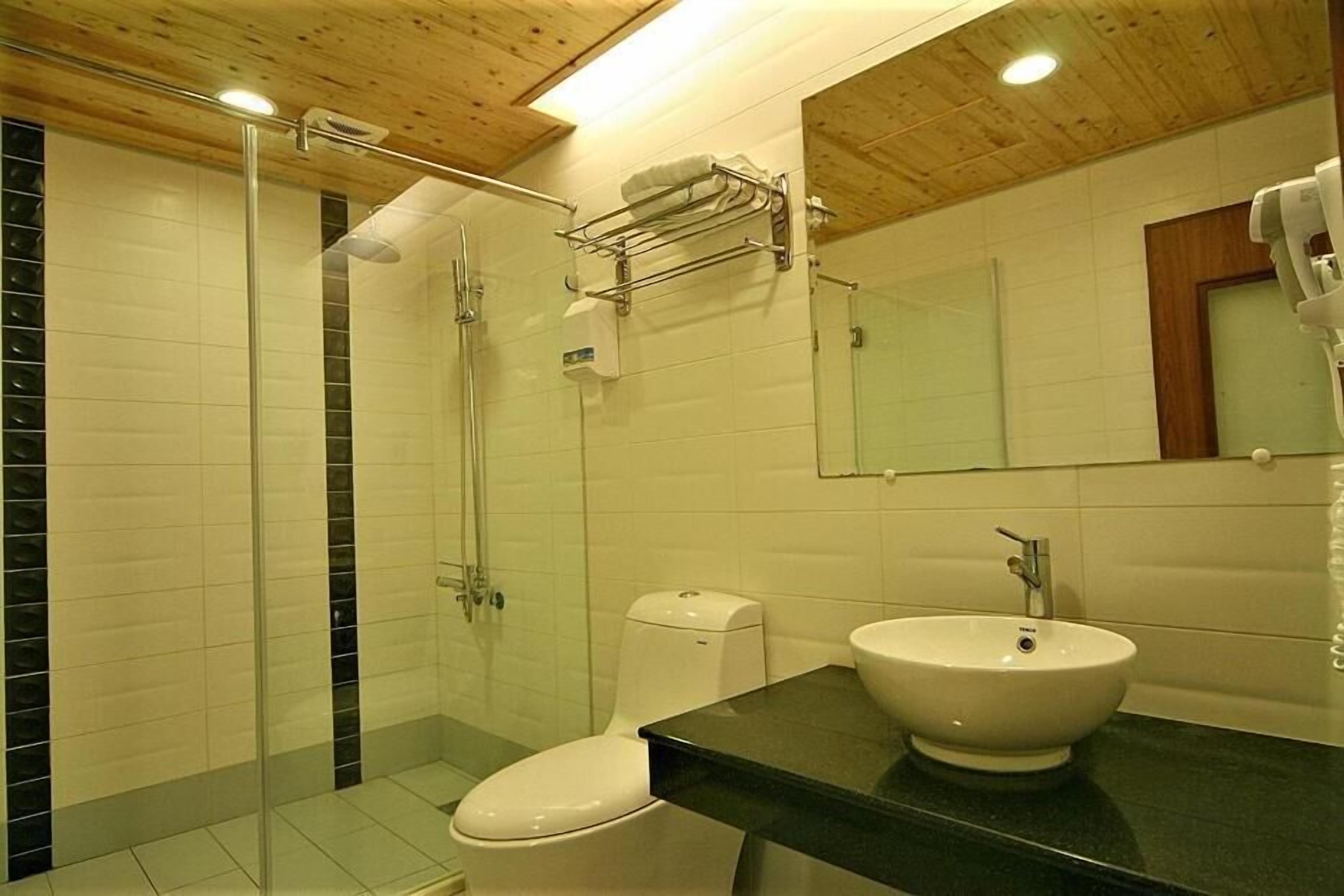 A modern bathroom with a glass shower enclosure, a white toilet, a black countertop, and a sink.