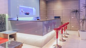 A modern bar area with a glass counter, red bar stools, and a decorative wall with a recessed shelf. - Tranquil Sea Hotel (Hengchun)