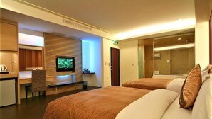 A hotel room with two beds, a desk with a chair, a television, and a bathroom visible through a glass door. - Tranquil Sea Hotel (Hengchun)