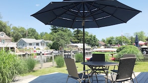A deck with a table and chairs, an umbrella, and a view of a marina with boats and houses. - Luxury Gun Lake 4 Bed 2 Bath Home W/paddleboards/kayaks, Free Wi-fi (Wayland)