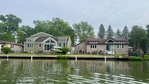 A row of houses by a calm lake, with docked canoes and a covered seating area. - Luxury Gun Lake 4 Bed 2 Bath Home W/paddleboards/kayaks, Free Wi-fi (Wayland)