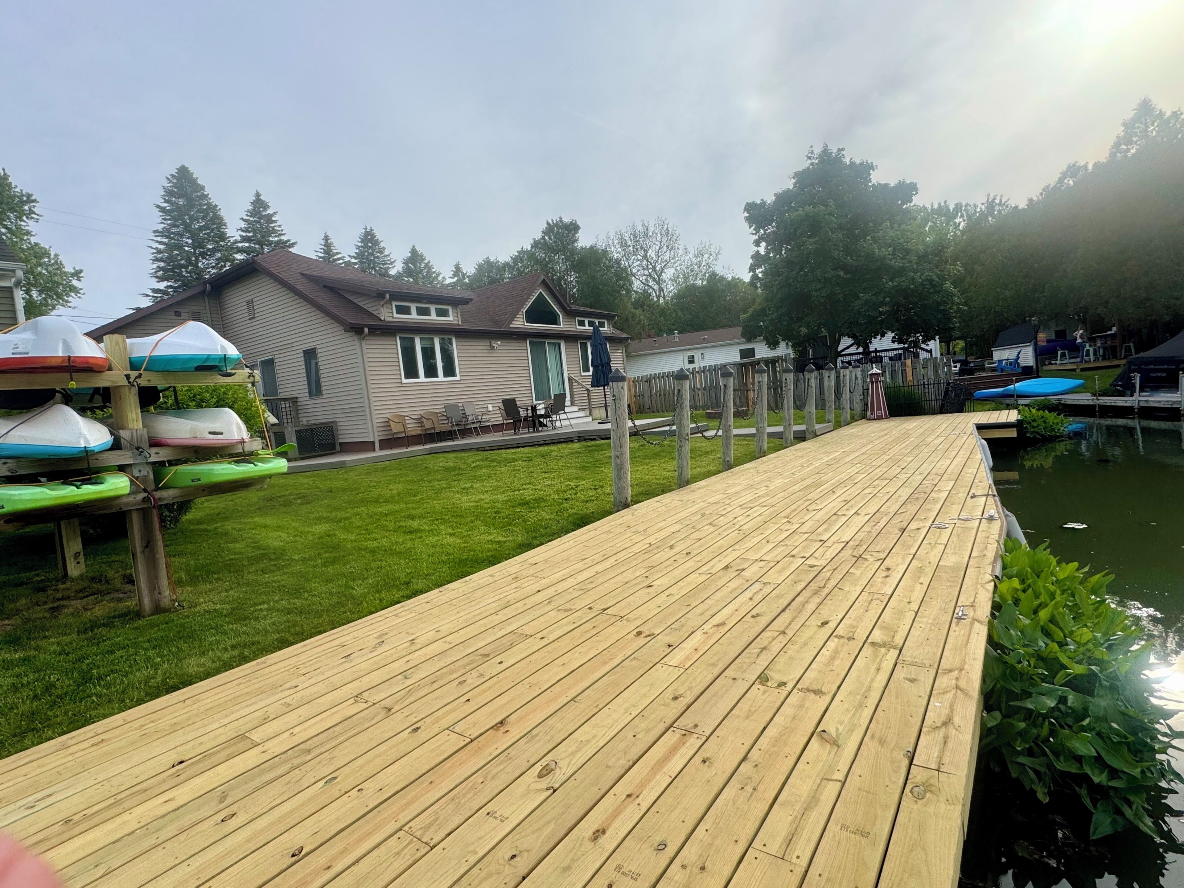 A wooden dock leading to a house with a fenced yard and a small body of water.