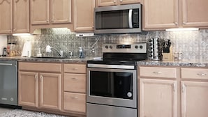 A modern kitchen with wooden cabinets, stainless steel appliances, and a patterned backsplash. - Luxury Gun Lake 4 Bed 2 Bath Home W/paddleboards/kayaks, Free Wi-fi (Wayland)