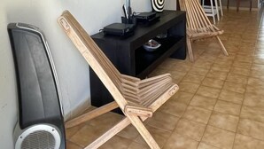 A living area with a flat-screen TV mounted on the wall, a black entertainment unit, and two wooden lounge chairs. - RELAX APART IN SPECIAL RAIN FOREST ,BEACH ZONE (RIO GRANDE)