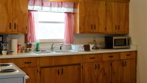 Une cuisine avec des meubles en bois, un four à micro-ondes, un évier et une fenêtre ornée d’un rideau à carreaux.