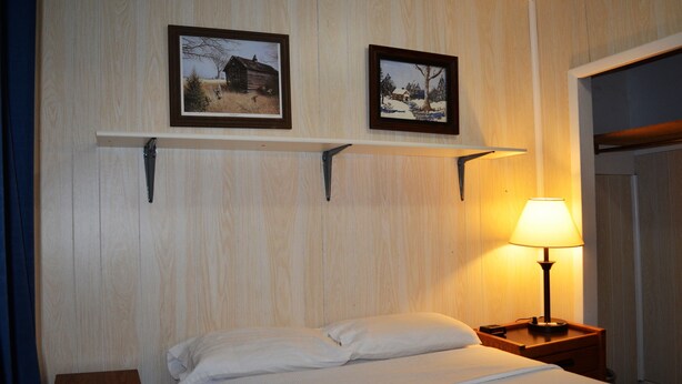 Une chambre d’hôtel avec un lit, une table de chevet avec une lampe et deux tableaux encadrés au mur.