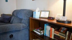 Une pièce avec un canapé bleu, une bibliothèque en bois remplie de livres, un certificat encadré, une horloge et une lampe.