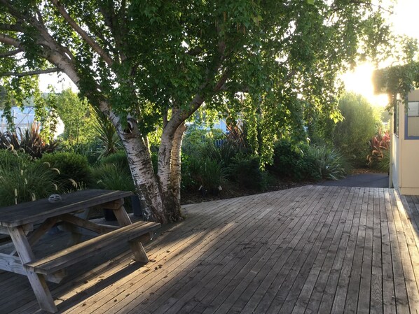 A wooden deck with a picnic table, surrounded by lush greenery and trees. - Stay in School by the Sea (Dunedin Area)
