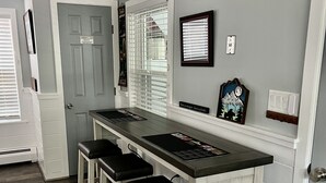 Cozinha com bancada central ampla, três banquetas de bar e janela com persianas.