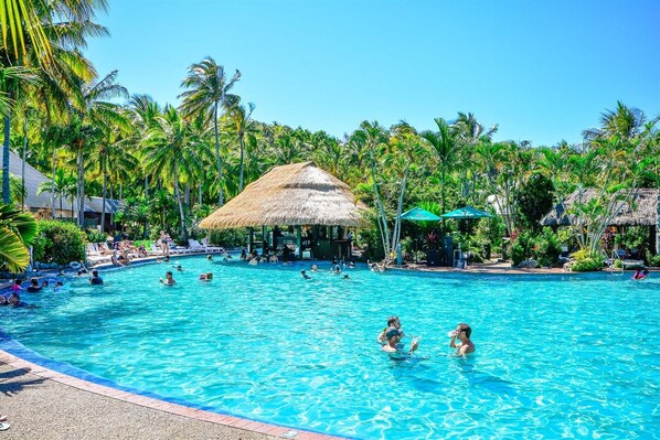 A swimming pool surrounded by palm trees and thatched-roof structures.