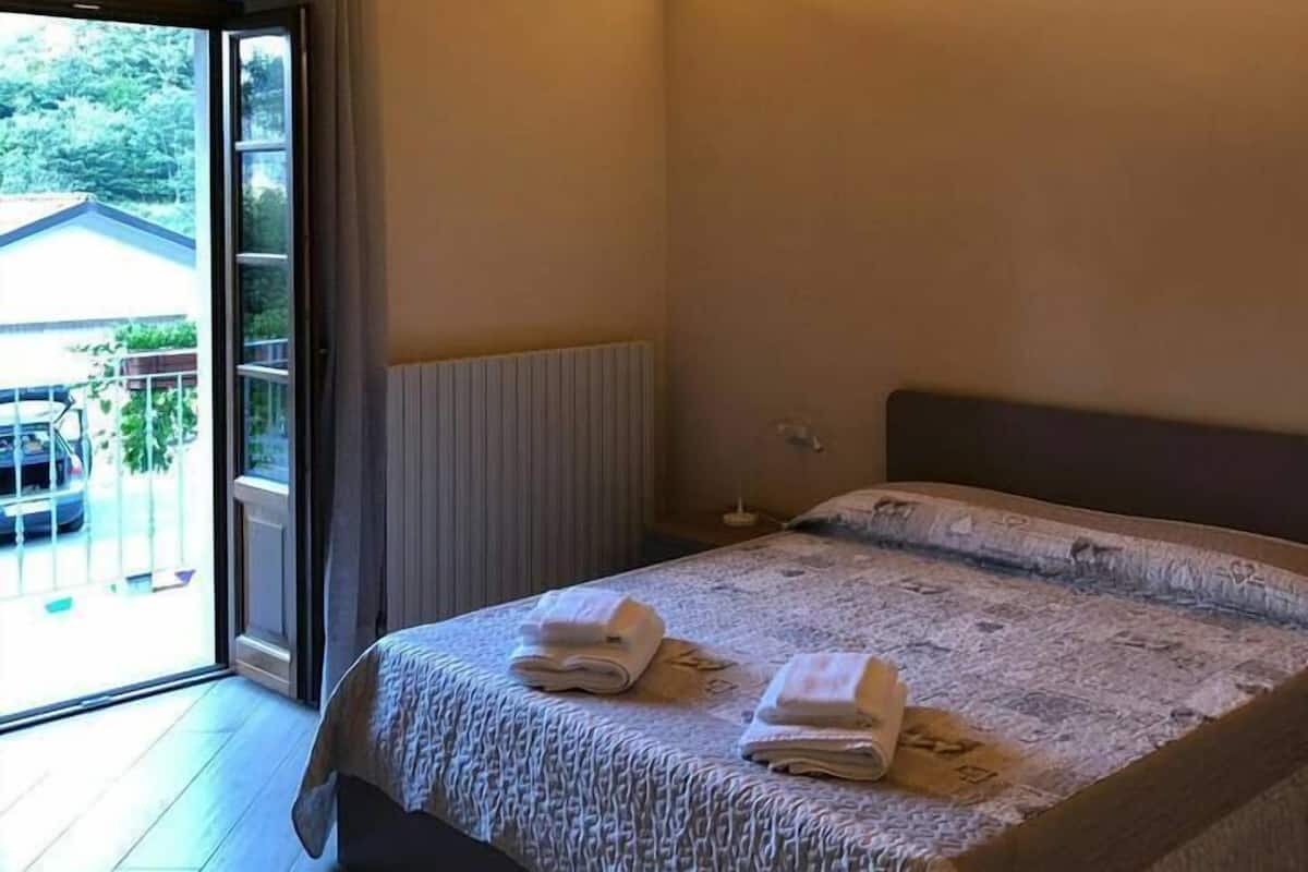 Une chambre avec un plafond en bois, un lit recouvert d’une courtepointe à motifs et une vue sur une voiture et la verdure à l’extérieur.