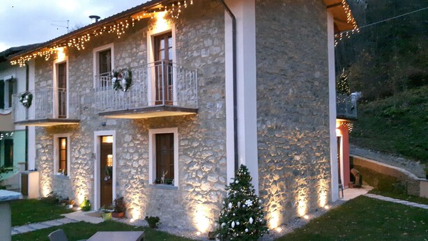 A stone building with a balcony, a small Christmas tree, and outdoor seating. - B&B da Morena (Minucciano)
