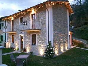 A stone building with a balcony, a small Christmas tree, and outdoor seating. - B&B da Morena (Minucciano)