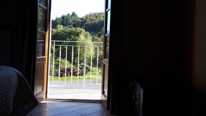 A room with a large sliding glass door leading to a balcony with a view of a forested hillside. - B&B da Morena (Minucciano)