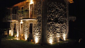 A stone building with a balcony and a small garden area with chairs and potted plants. - B&B da Morena (Minucciano)