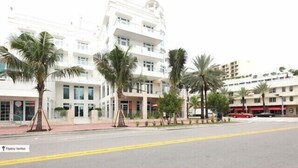 Un hotel de varios pisos con fachada blanca, palmeras en la entrada y una carretera despejada con línea amarilla.