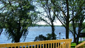 Une terrasse en bois avec une balustrade donnant sur un lac, entourée d’arbres.