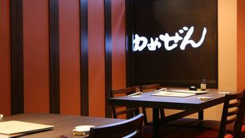 Ein Restaurantinneres mit Holztischen und einer dunklen Wand, die mit beleuchteten japanischen Schriftzeichen versehen ist.