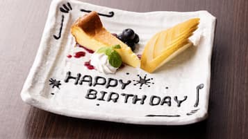A dessert plate with a slice of cheesecake, blueberries, and a leaf-shaped pastry on a white plate with "HAPPY BIRTH DAY" written in chocolate.