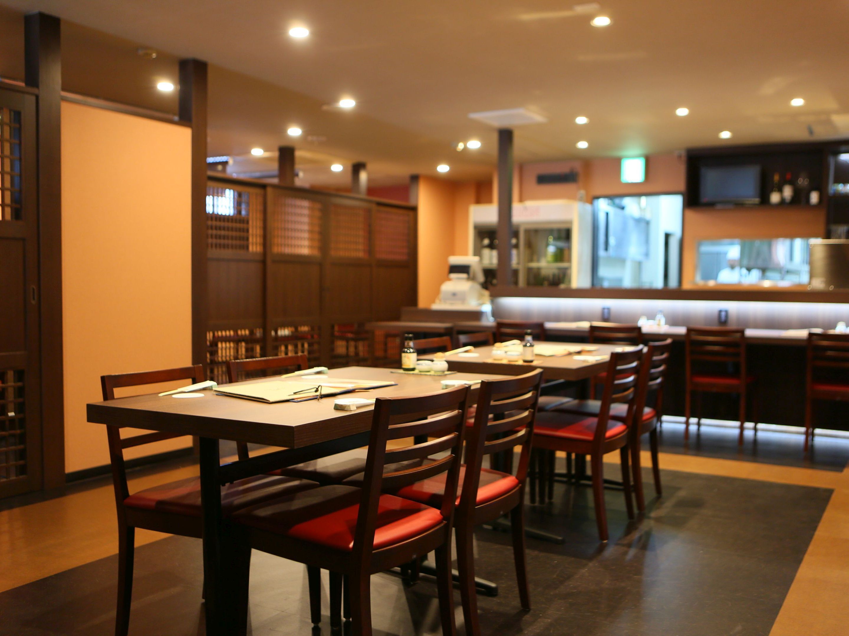 A restaurant with multiple tables and chairs, a counter, and a kitchen area.