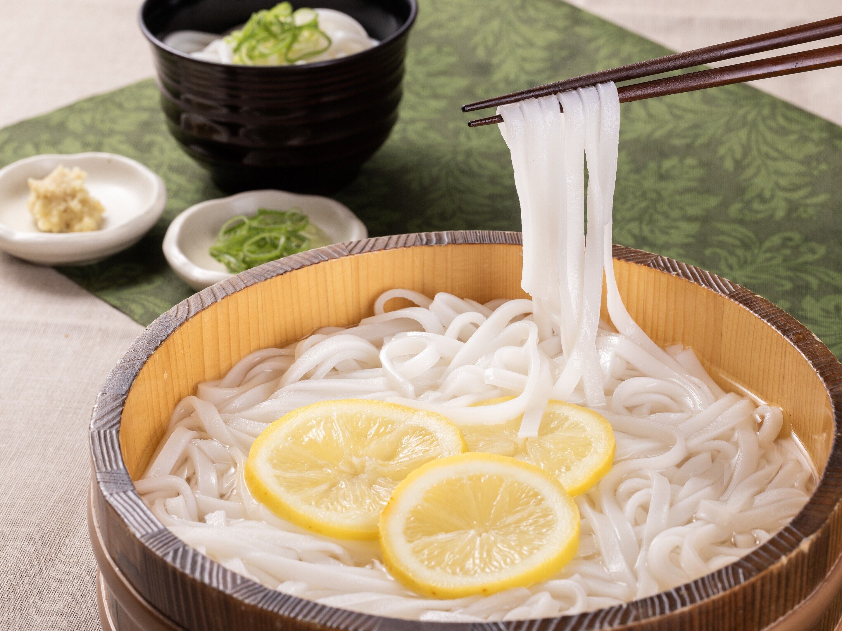 A bowl of noodles with lemon slices and chopsticks.