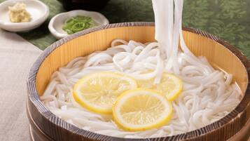 A bowl of noodles with lemon slices and chopsticks.