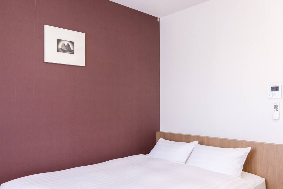 Ein Hotelzimmer mit einem Bett, einem an der Wand montierten Thermostat und einem gerahmten Bild.