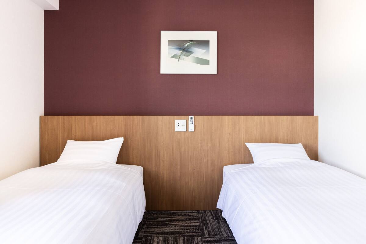Ein Hotelzimmer mit zwei Betten, einem hölzernen Kopfstück, einer roten Wand und einem Bild im Rahmen über den Betten.
