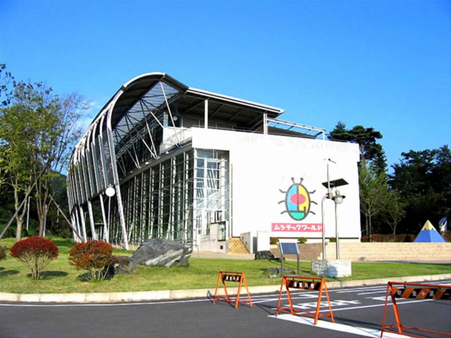 A modern building with a curved glass facade, a large entrance, and a sign with a colorful logo.