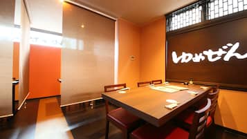 A conference room with a wooden table, red chairs, and a large screen with Japanese text.