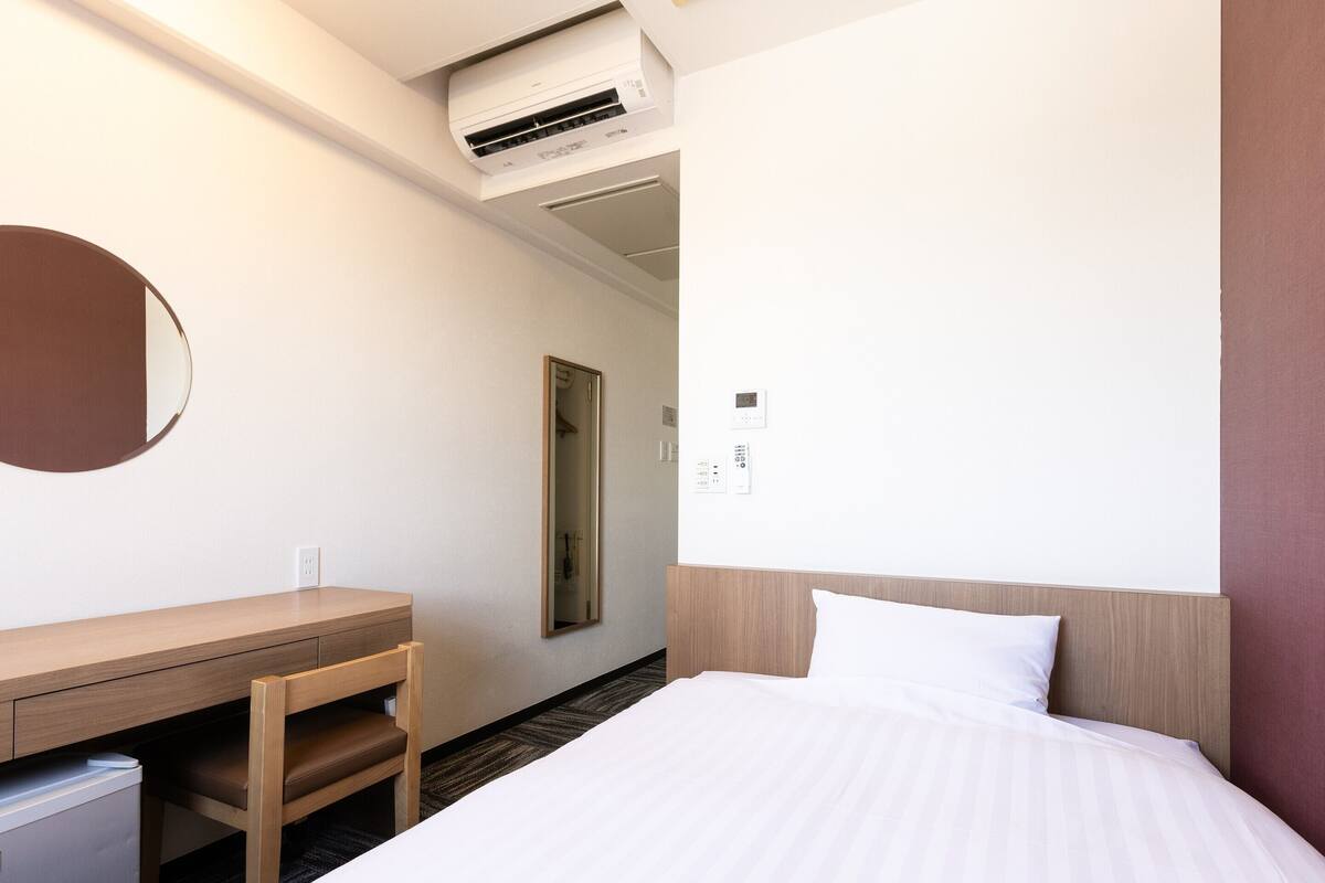 Ein Hotelzimmer mit Bett, Schreibtisch, Spiegel und Klimaanlage.