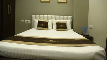 A hotel room with a large bed, a headboard, two framed pictures on the wall, and a bedside table with a water bottle.