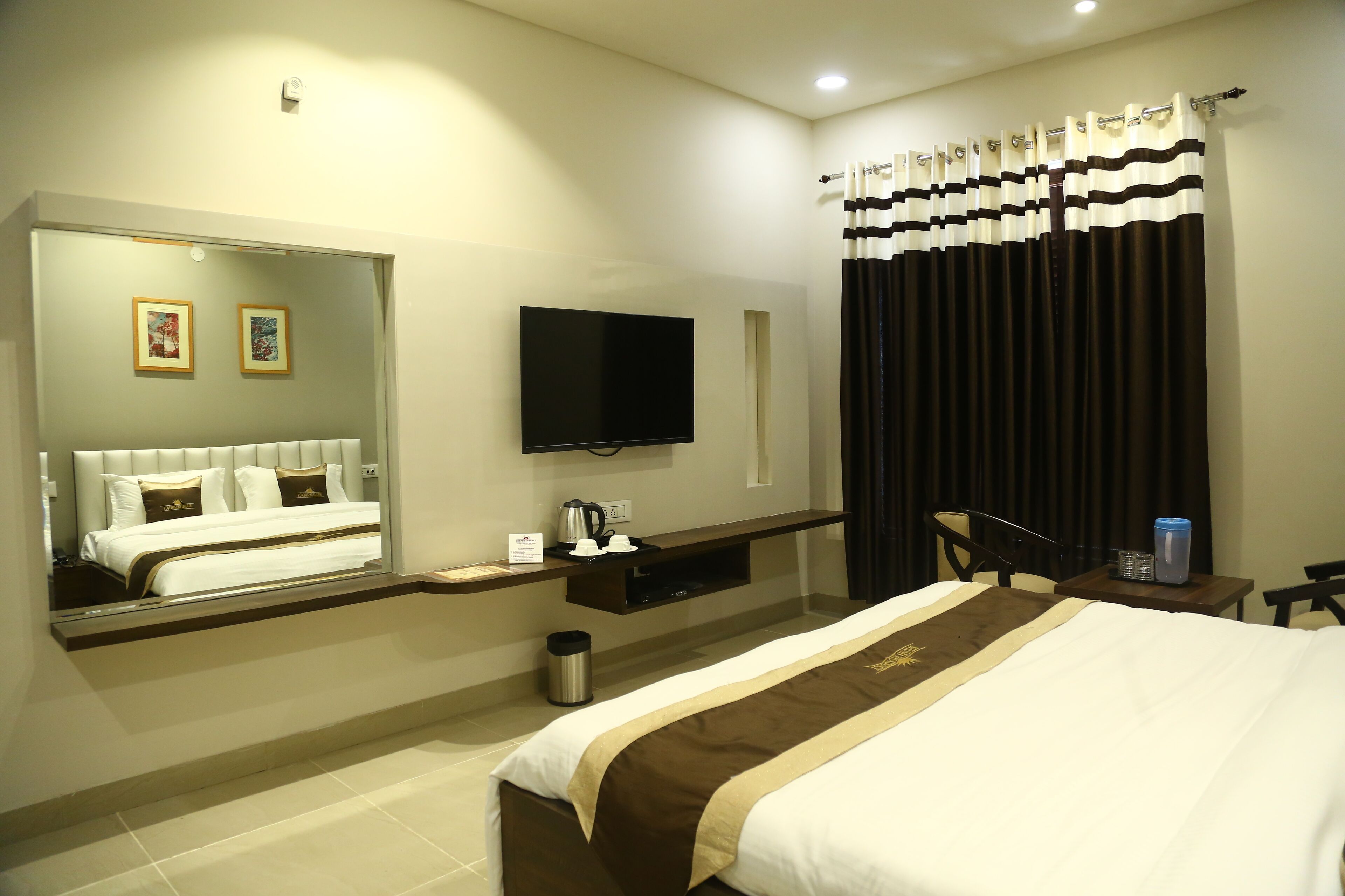 Habitación de hotel con una cama grande, televisor de pantalla plana, escritorio con silla, espejo y ventana con cortinas.