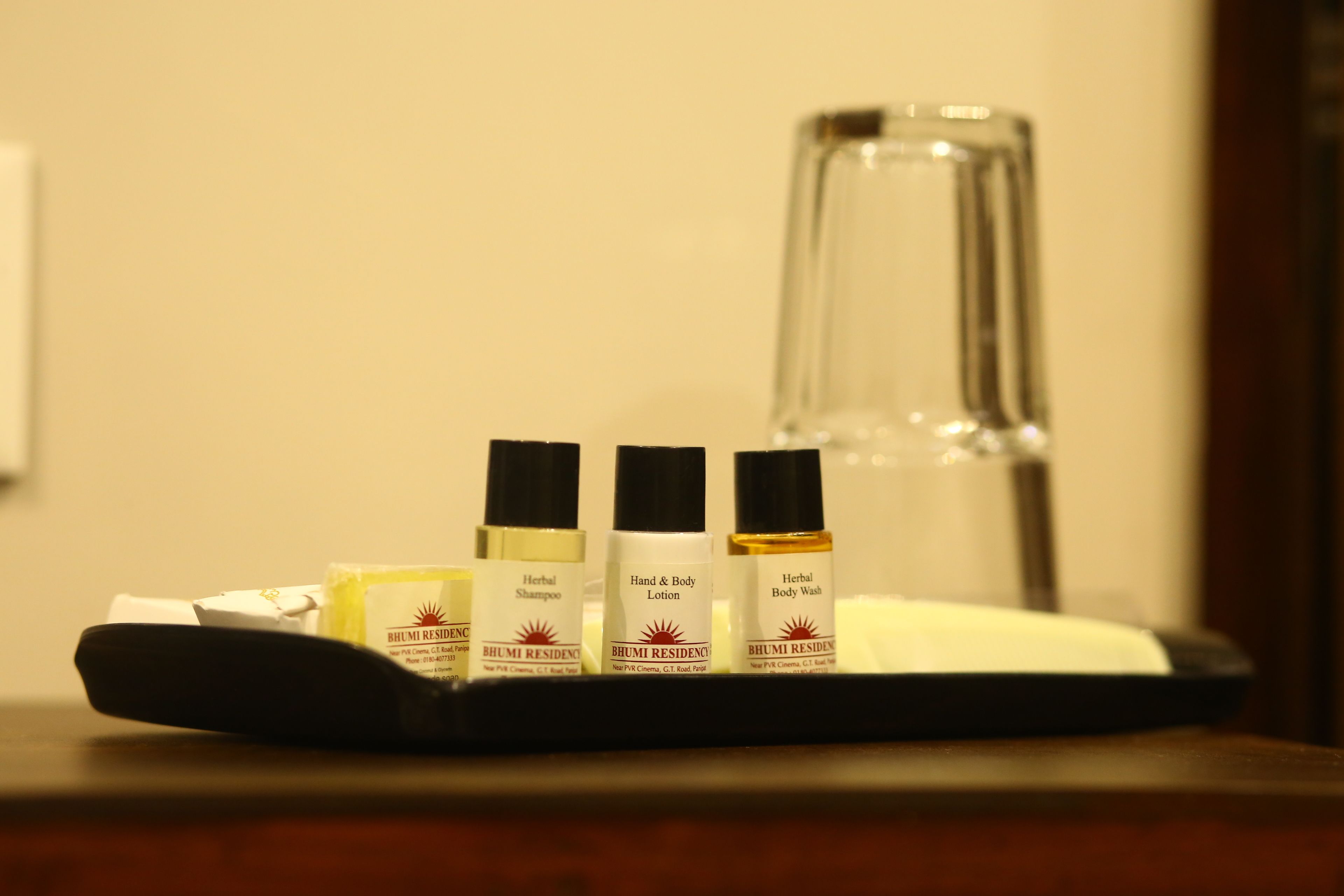 A tray with three bottles of BHUMI RESIDENCE products and a glass bottle on a wooden surface.