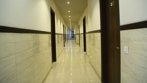 A long, well-lit hallway with marble walls and doors, leading to a room.