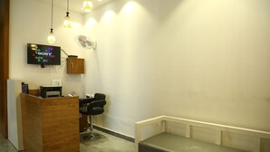 A reception area with a wooden desk, a black office chair, a bench, a wall-mounted TV, and a fan.