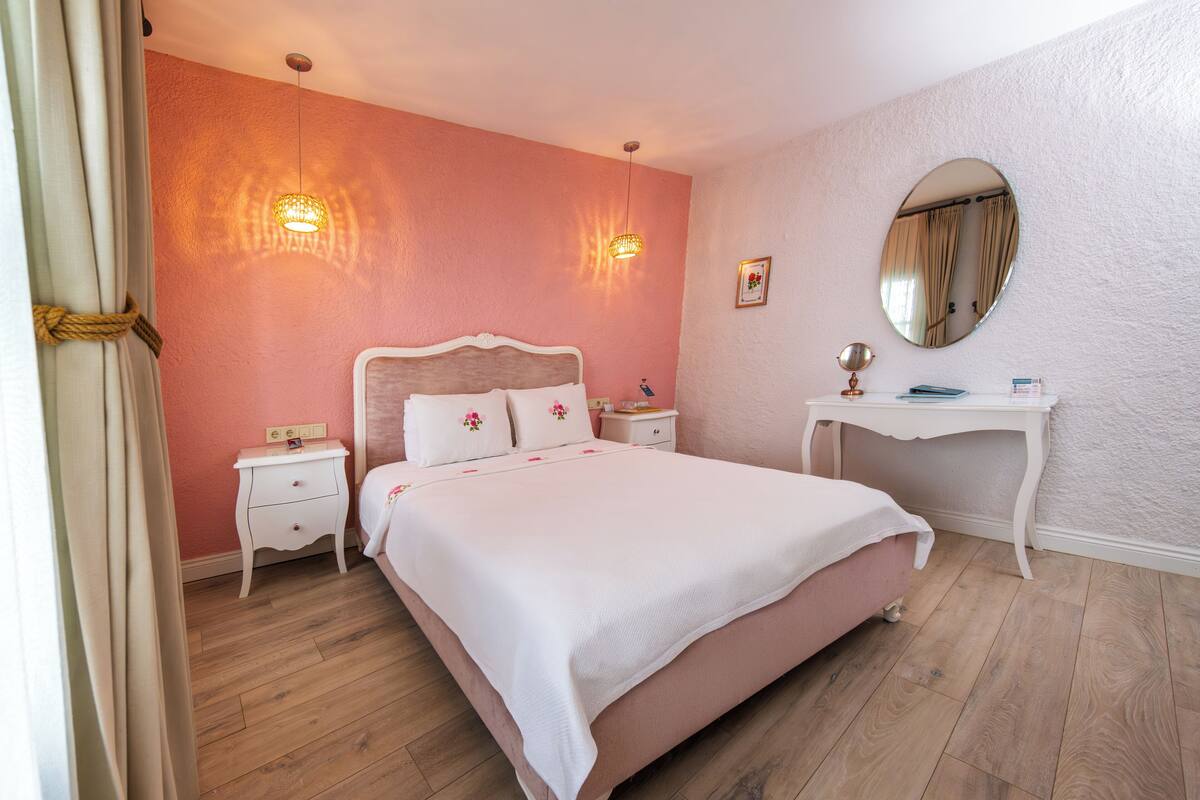 Un dormitorio con cama, mesitas de noche, escritorio, espejo y una lámpara fijada a la pared.