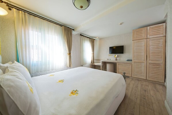 Une chambre d’hôtel avec un grand lit, un bureau, une télévision et des armoires en bois.