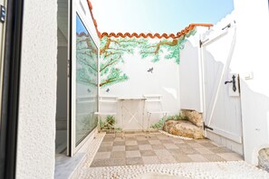 Un espace patio doté d’un sol carrelé, d’un mur blanc orné d’une fresque, d’un portail blanc et d’une petite table avec des chaises.