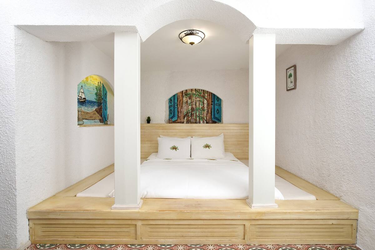 Un dormitorio con estructura de cama de madera, ropa de cama blanca y un cabecero decorativo.